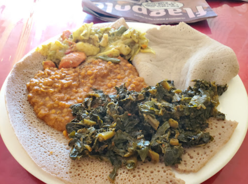 A plate of Ethiopian food featuring injera, lentil stew, sautéed vegetables, and collard greens.
