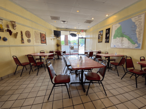 A spacious restaurant interior with red chairs, wooden tables, and wall decor, including maps and cultural artifacts.