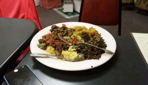 A plate of food featuring yellow rice, beef with vegetables, and dark greens, served with two forks on a table.