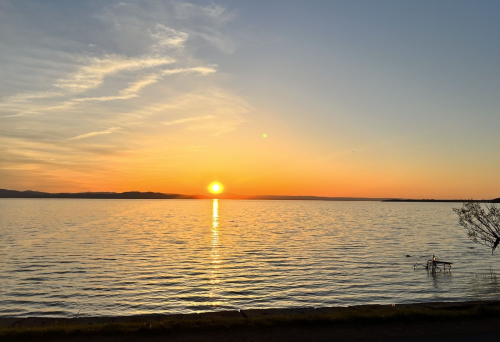 A serene sunset over a calm lake, with warm orange and yellow hues reflecting on the water's surface.