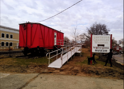 A red train car on a grassy area next to a sign for the Gertrude Chandler Warner Museum, with a ramp for access.