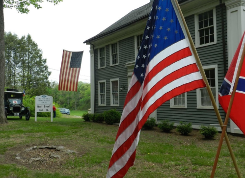 Two flags, one American and one Norwegian, are displayed outside a gray building with a sign for an event.