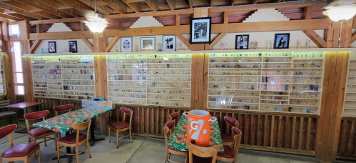 A wooden interior with a display wall filled with collectibles, surrounded by tables and chairs.