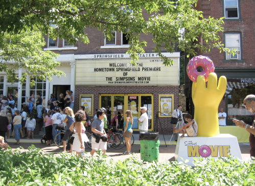 Crowd gathers outside a theater for the hometown premiere of "The Simpsons Movie," featuring a large donut statue.