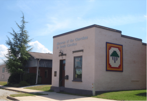 Exterior view of the Museum of the Cherokee in South Carolina, featuring a colorful logo and surrounding greenery.