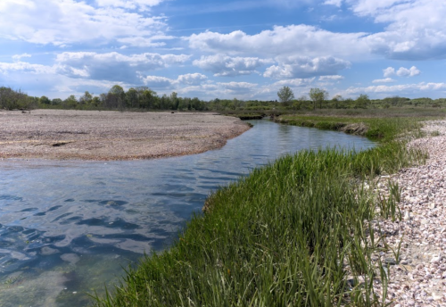 A serene river winding through a grassy bank under a blue sky with fluffy clouds.