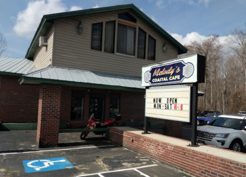 Exterior of Melody's Coastal Cafe with a sign indicating hours, featuring a brick facade and a motorcycle parked outside.