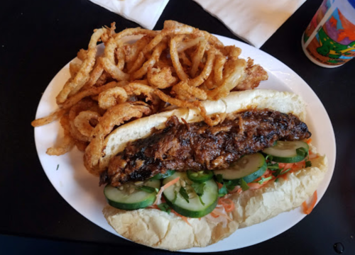 A plate featuring a grilled sandwich with vegetables and a side of crispy onion rings.