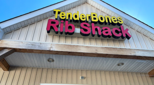 Sign for "TenderBones Rib Shack" on a wooden building with a clear blue sky above.
