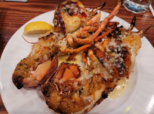 A plate of grilled lobster tails topped with cheese, served with a lemon wedge.