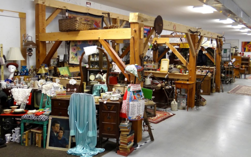 A cozy antique shop filled with vintage items, furniture, and decor displayed on wooden shelves and tables.