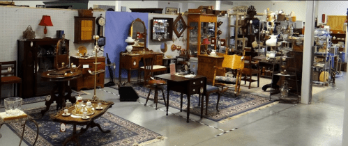 A spacious antique shop filled with various vintage furniture and decor items, arranged on a polished floor.