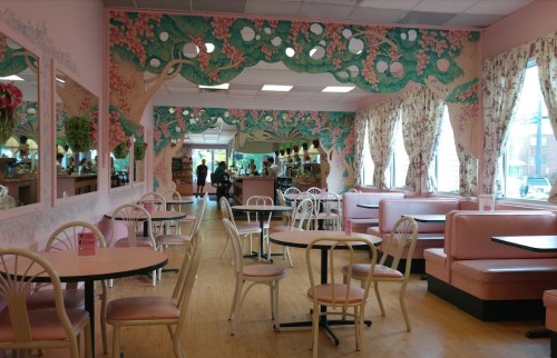 A pastel-colored café interior with floral murals, pink booths, and round tables, creating a cozy atmosphere.