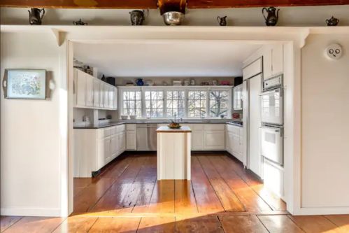 Bright, spacious kitchen with white cabinets, a central island, and large windows overlooking a wooded area.