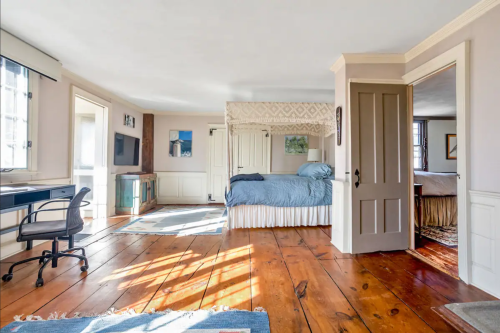 Spacious bedroom with a blue bedspread, wooden floors, and natural light from large windows.