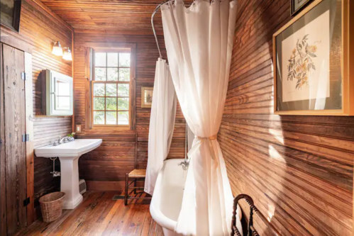 Cozy bathroom with wooden walls, a vintage bathtub, and natural light from a window.