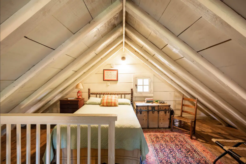 Cozy attic bedroom with a bed, wooden furniture, and a colorful rug under a sloped ceiling.