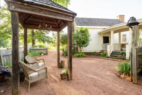 A cozy outdoor space featuring a gazebo, chairs, and lush greenery beside a charming white house.