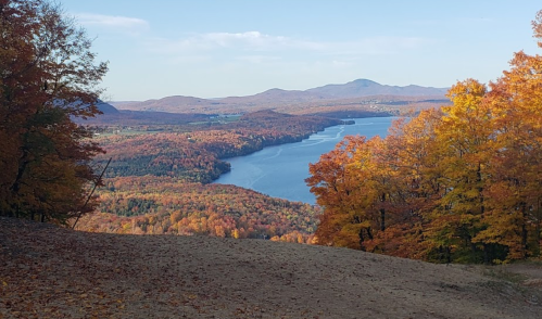 A scenic view of a lake surrounded by vibrant autumn foliage and distant mountains under a clear blue sky.