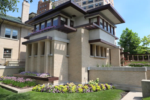 A modernist building with a unique design, featuring large windows and a landscaped garden with colorful flowers.