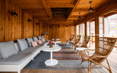 Cozy wooden patio with seating, tables, and decorative flowers, creating a warm and inviting atmosphere.
