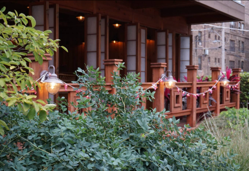 A wooden building with lanterns and greenery in the foreground, creating a cozy outdoor atmosphere.