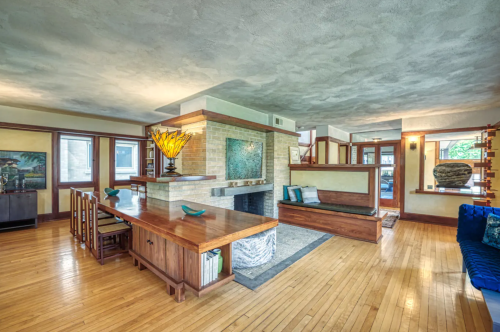 Spacious living area with wooden furniture, a central fireplace, and large windows, featuring a cozy dining space.