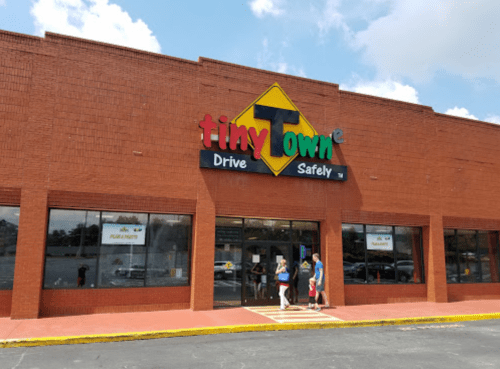 Exterior of a building with a colorful sign reading "Tiny Town" and people entering the store on a sunny day.