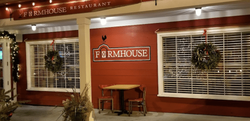 Exterior of the Farmhouse Restaurant, featuring festive wreaths and warm lighting on a red wooden facade.