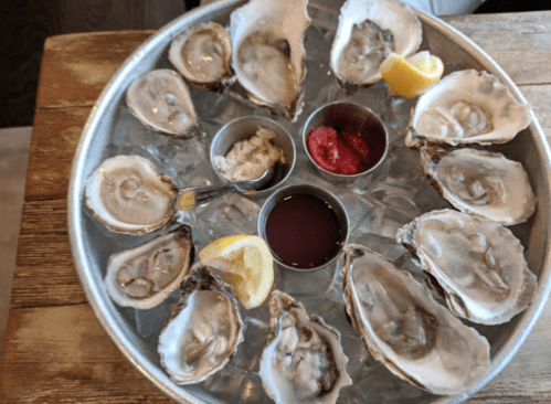 A platter of fresh oysters on ice, served with lemon wedges and dipping sauces.