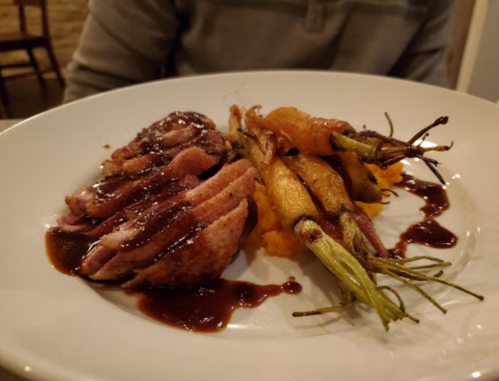 A plate featuring sliced duck breast with a rich sauce, served alongside roasted carrots and a bed of mashed sweet potatoes.