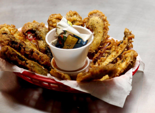 A basket of crispy fried food with a small cup of dipping sauce in the center.