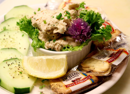 A plate with cucumber slices, lettuce, a bowl of spread topped with chives, a lemon wedge, and crackers.