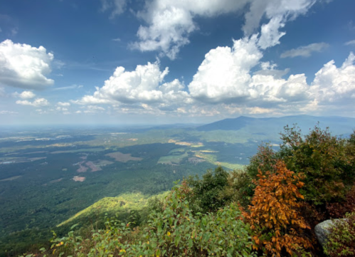 A panoramic view of lush green mountains and valleys under a blue sky with fluffy white clouds.