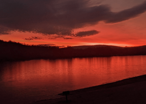 A serene sunset over a calm river, with vibrant red and orange hues reflecting on the water's surface.