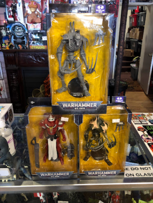 Three Warhammer action figures in packaging, displayed in a store with a colorful background of collectibles.