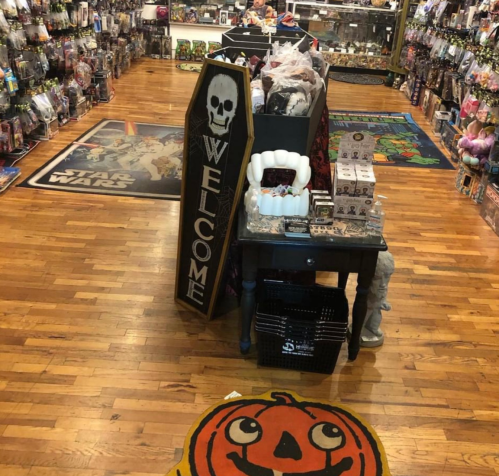 A spooky store interior with Halloween decorations, including a coffin sign and a smiling pumpkin rug.