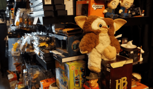 A shelf filled with various toys and collectibles, featuring a plush Gremlin in the foreground.