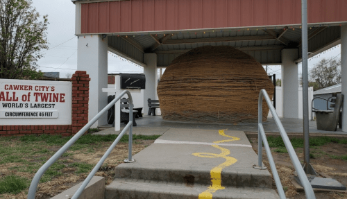 A large ball of twine displayed under a shelter in Cawker City, with a sign indicating it's the world's largest.