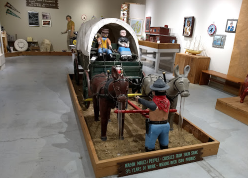 A diorama featuring a covered wagon with figures and horses, showcasing craftsmanship and historical themes.