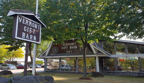 A rustic building with a sign reading "Vermont Gift Barn" surrounded by trees and parked cars.