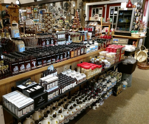 A well-stocked store display featuring various bottles of syrup, sauces, and condiments on wooden shelves.