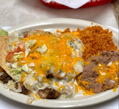 A plate of cheesy enchiladas topped with lettuce and tomatoes, served with rice and refried beans.