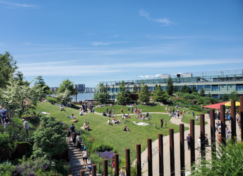 A vibrant park scene with people enjoying the outdoors on a sunny day, surrounded by greenery and modern buildings.