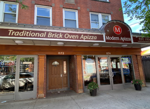 Exterior of Modern Apizza, featuring a brick facade and signage for "Traditional Brick Oven Apizza" in a city setting.