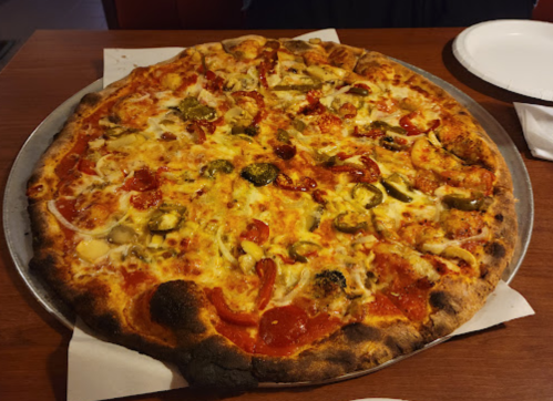 A large pizza topped with cheese, pepperoni, green peppers, onions, and pickles on a metal tray.