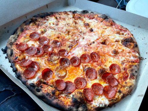 A large pepperoni pizza with melted cheese and a slightly charred crust, placed in a pizza box.