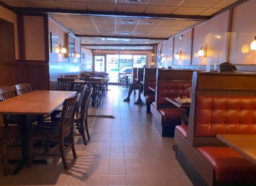 Interior of a restaurant featuring wooden tables, red booths, and a view of the entrance with a few patrons seated.