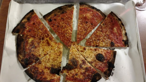 A partially sliced pizza with a crispy crust and burnt edges, arranged in a circular pattern on a white tray.