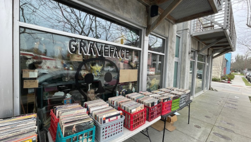 A storefront with the sign "GRAVEFACE" featuring tables of vinyl records displayed outside.
